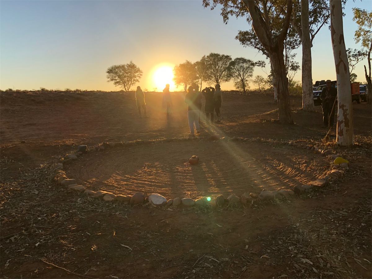 The sun setting over a ceremonial circle on red earth